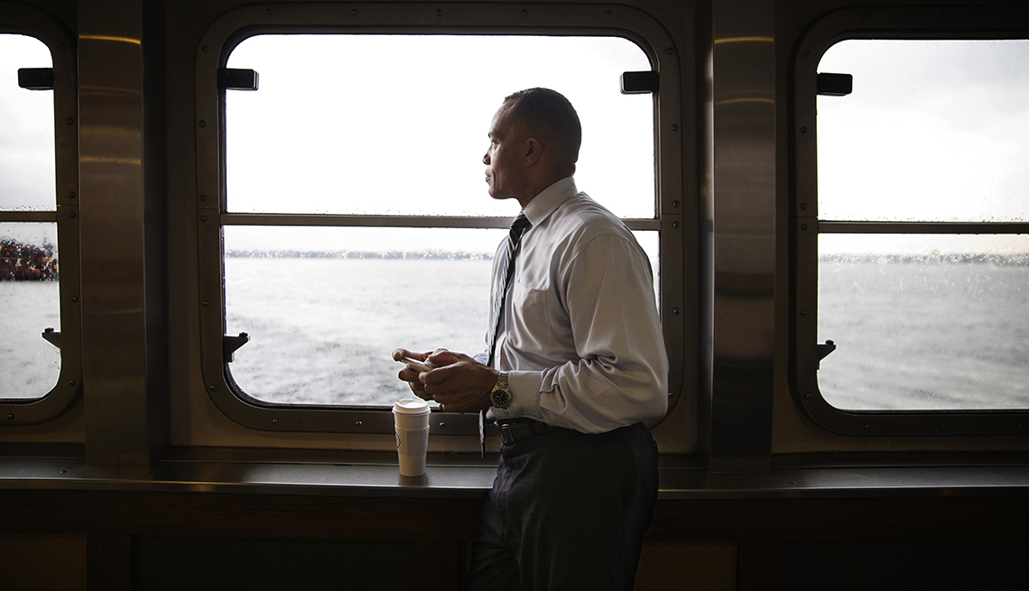 Businessman gazes out window of ferry building while using phone and having coffee